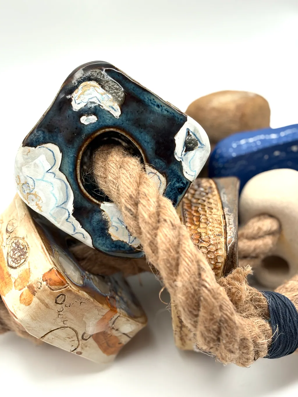 Close detail of Bluff/Spit/Drift: a dark blue glazed block with a white cloud, the rope passing through it.