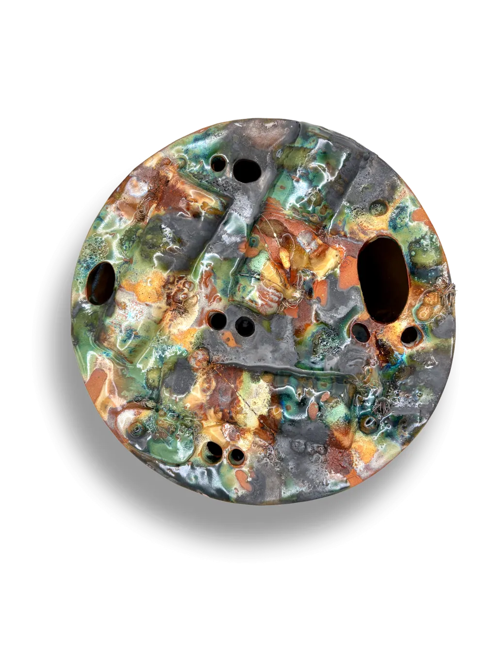 A round, heavily textured stoneware plate with pierced holes, glazed in mossy green, rust and slate.