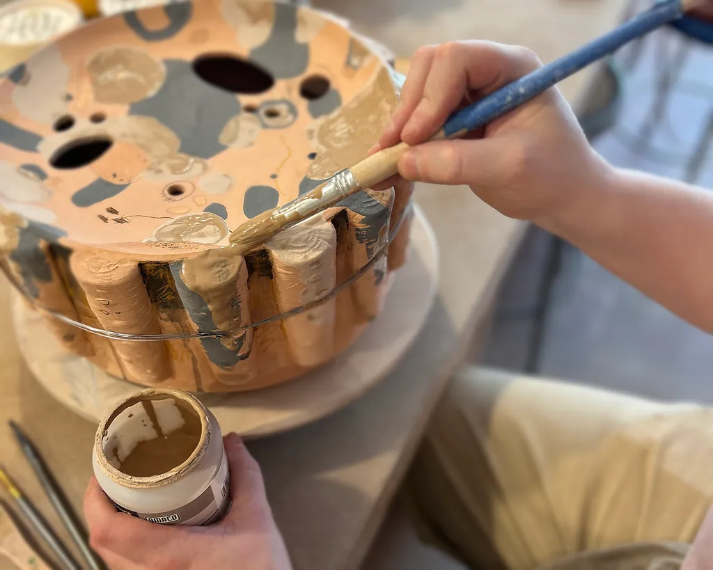 Hands brushing glaze onto a fluted, textured piece.