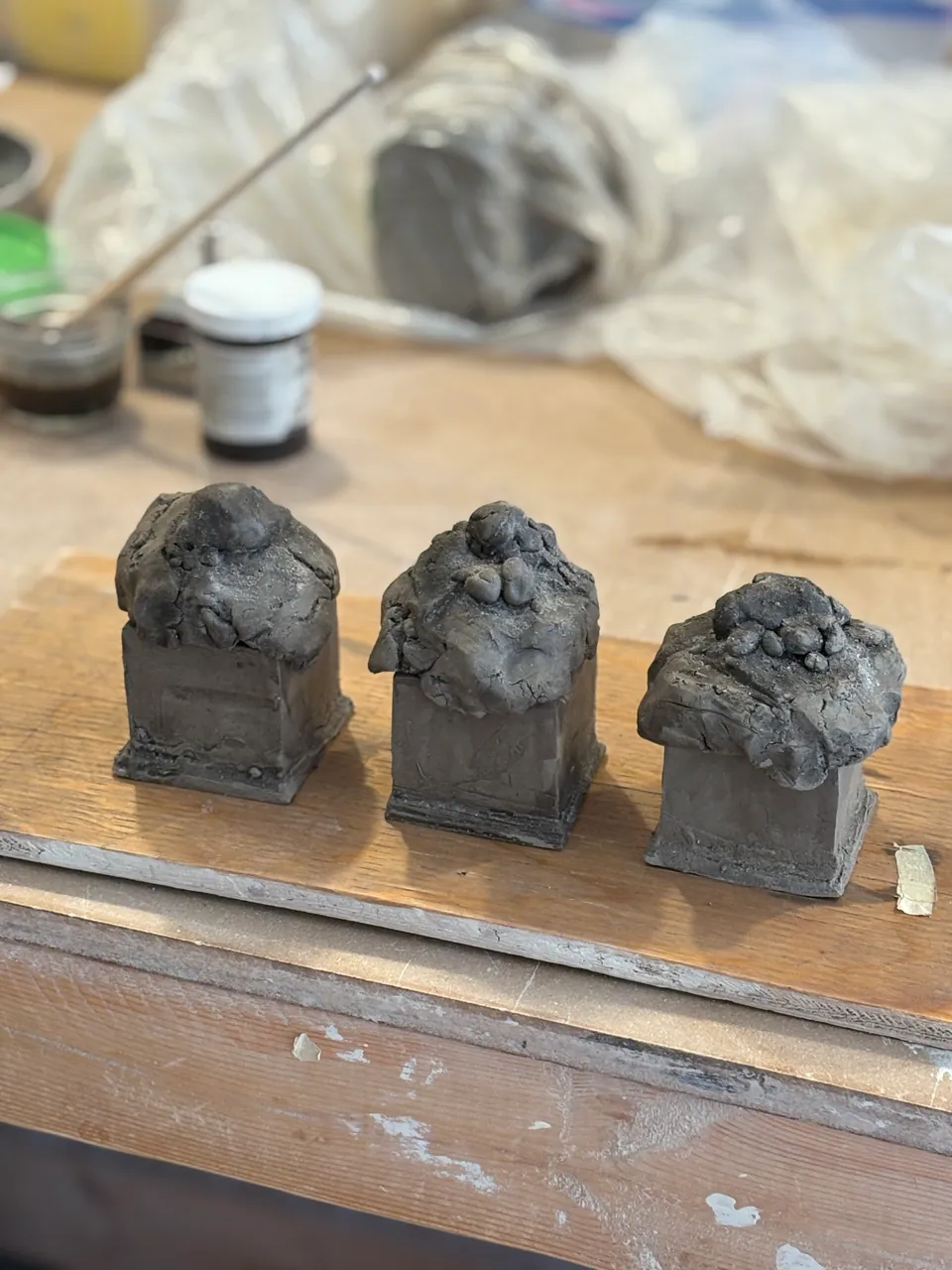 Three small unfired clay houses lined up on a banding wheel in the studio.