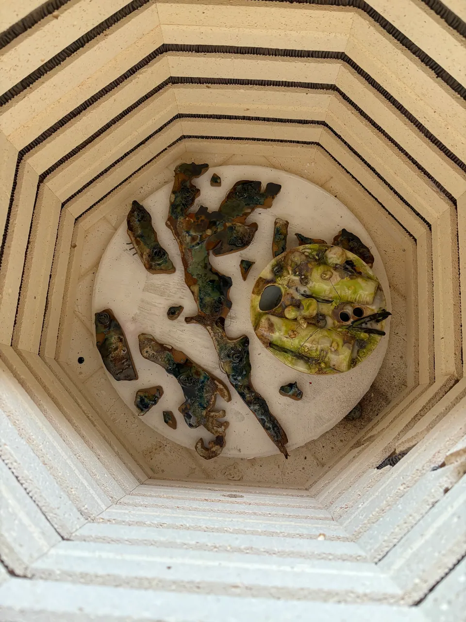 Looking down into a kiln at a piece resting on a shelf.