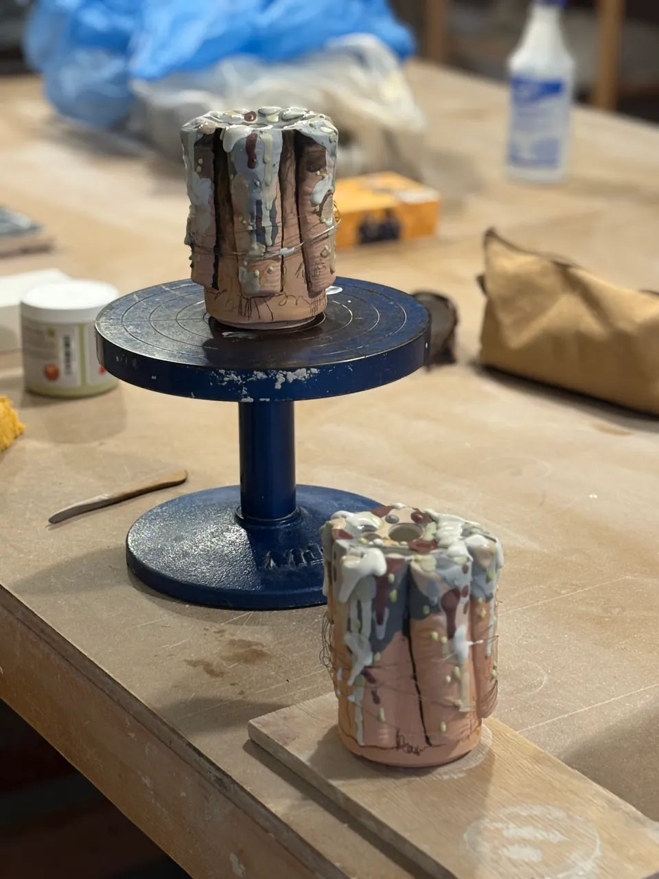 Bisque tubes standing on a banding wheel next to a glaze bucket.