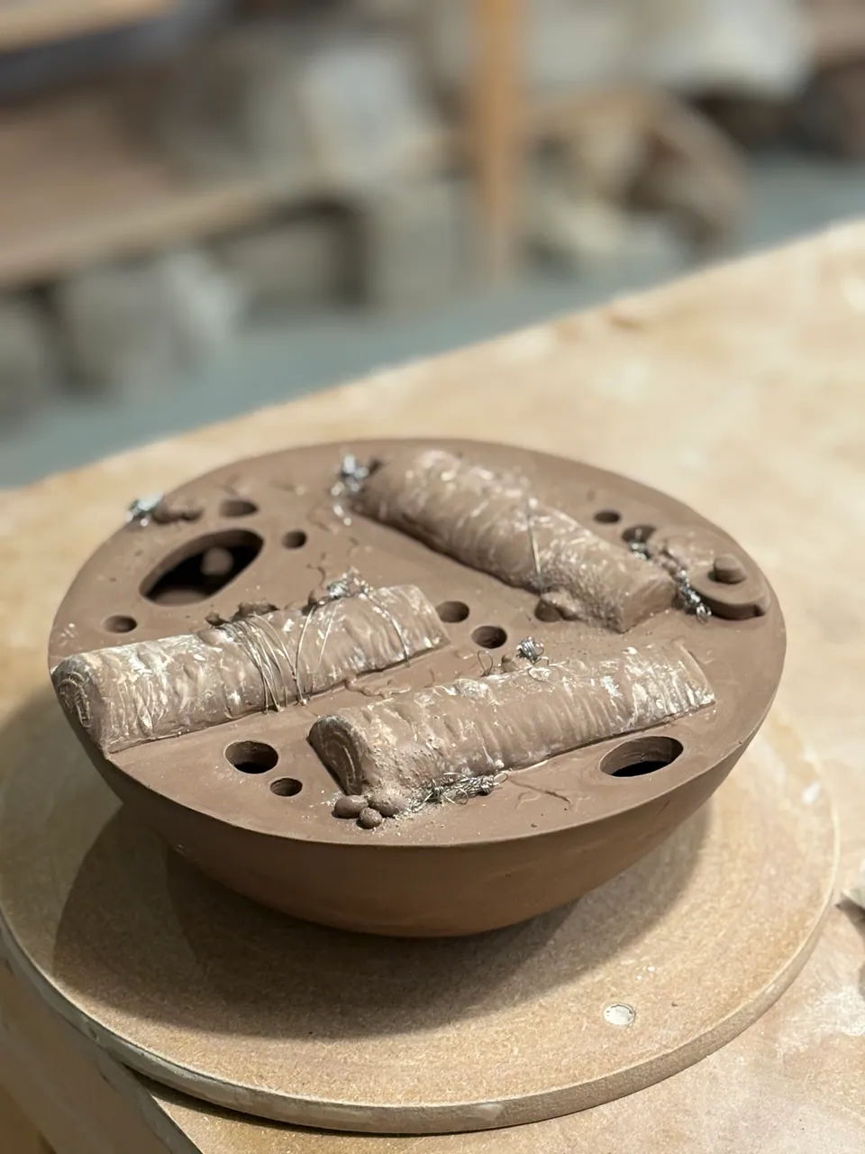A round textured stoneware form with holes, resting on the bench.