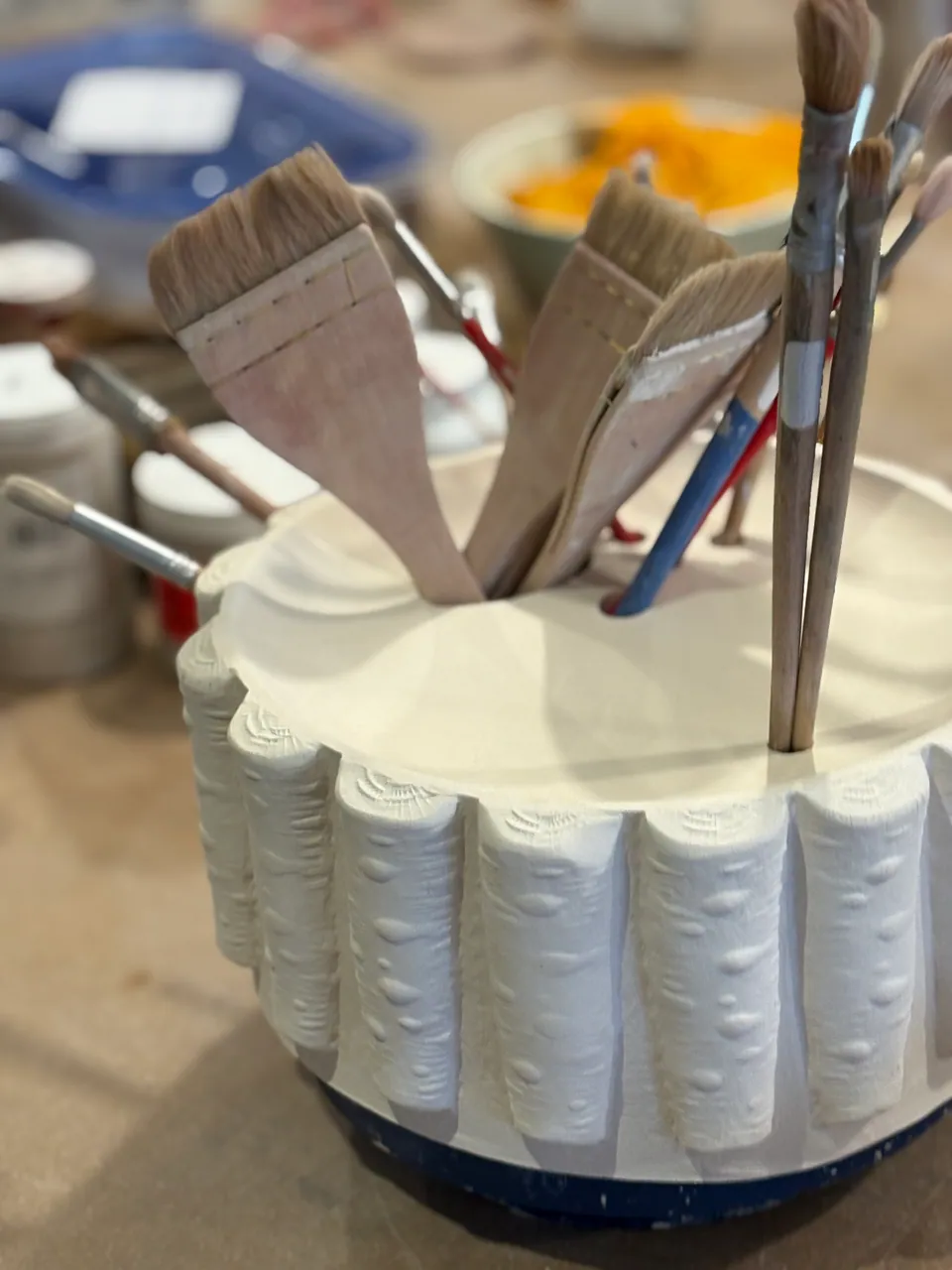 A white fluted bisque piece holding brushes and tools.