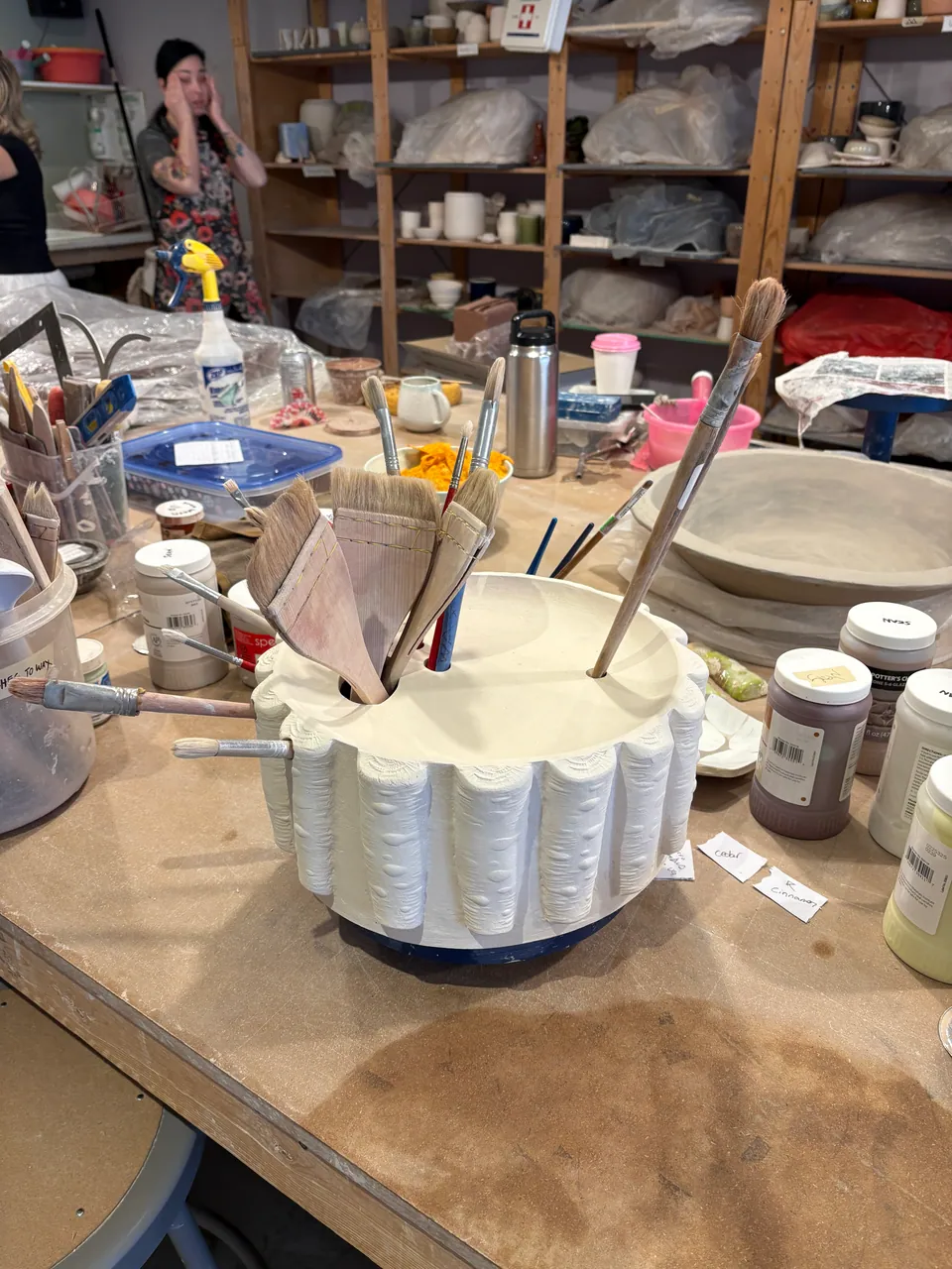 A fluted piece full of brushes in the middle of a busy studio.